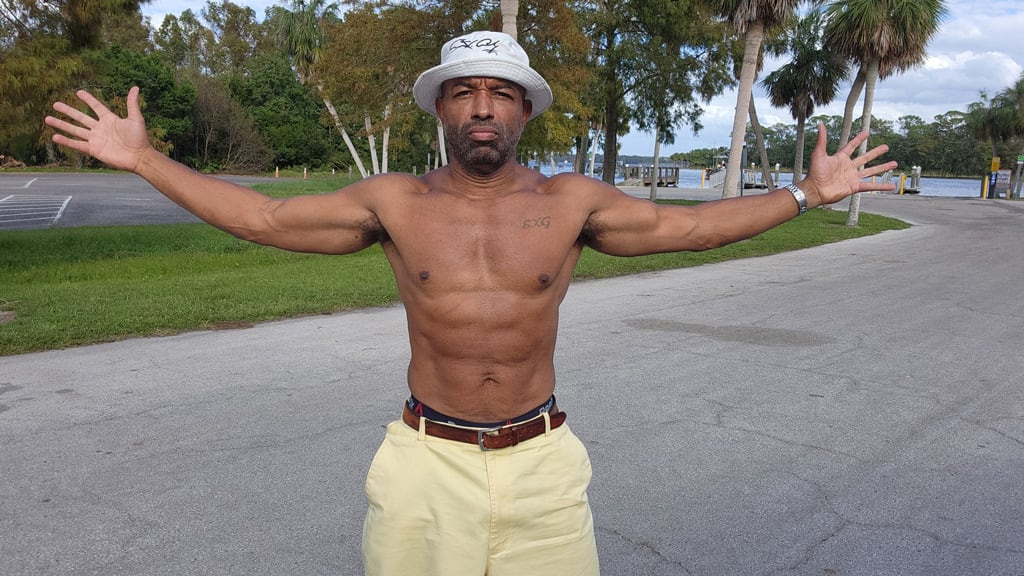 Coach is posing outdoors showing his abs.